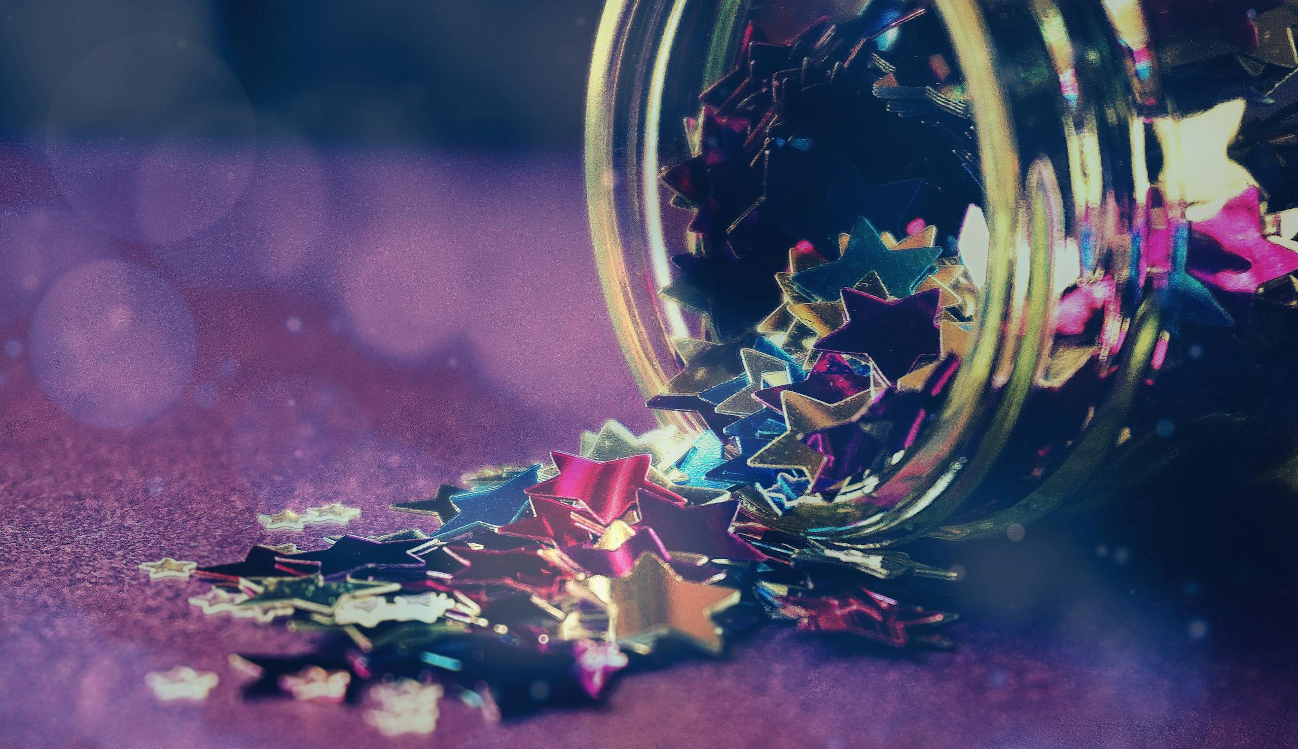 Colorful star-shaped confetti spilling out of a glass jar creates a festive and artistic scene.